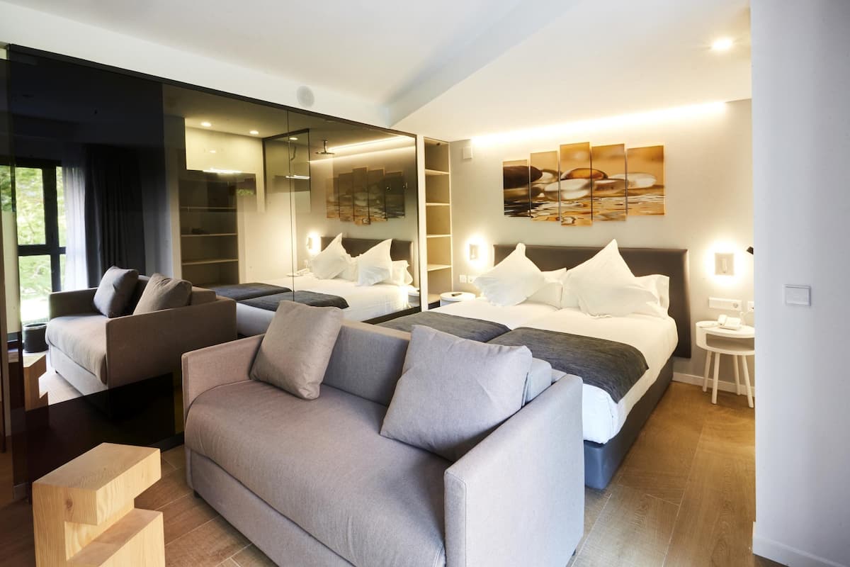 A modern bedroom with a large bed, a sofa, a desk, and a mirror.