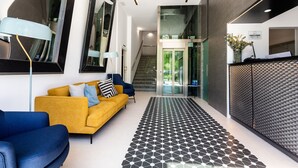 A modern lobby with a geometric patterned floor, a yellow sofa, blue armchairs, and a staircase leading to an upper level. - Moontels Valencia Alameda 41 (Valencia)