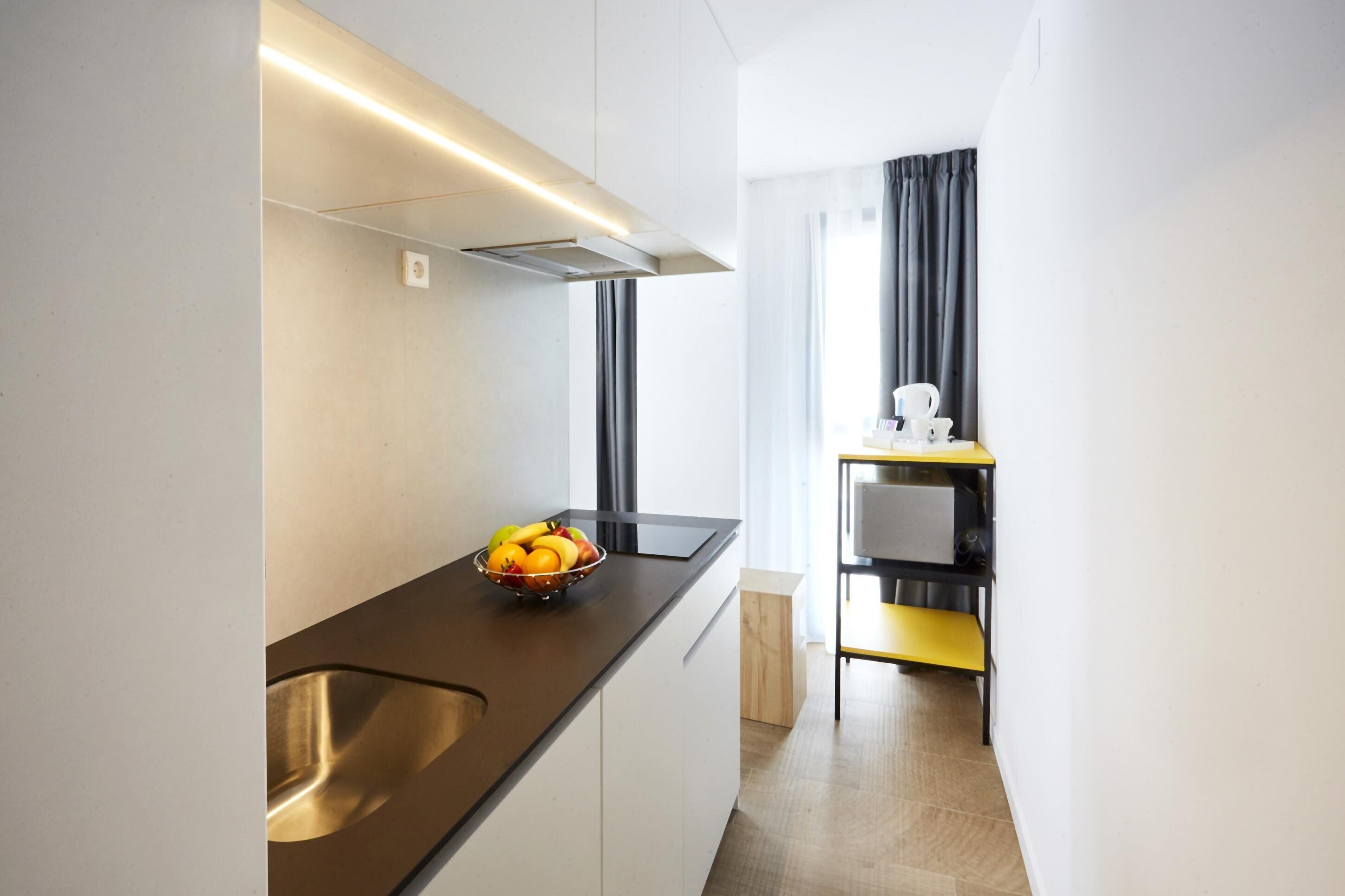 A modern kitchen with a stainless steel sink, a fruit bowl on the counter, and a built-in oven.