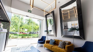 A modern reception area with a yellow sofa, blue armchairs, and a patterned rug. - Moontels Valencia Alameda 41 (Valencia)