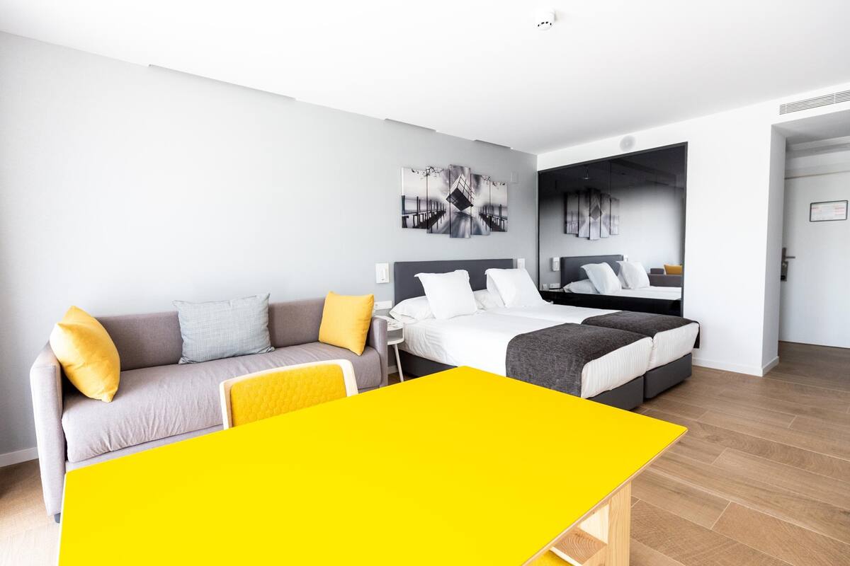 A modern hotel room with a bed, a sofa, a small table, and a large mirror.