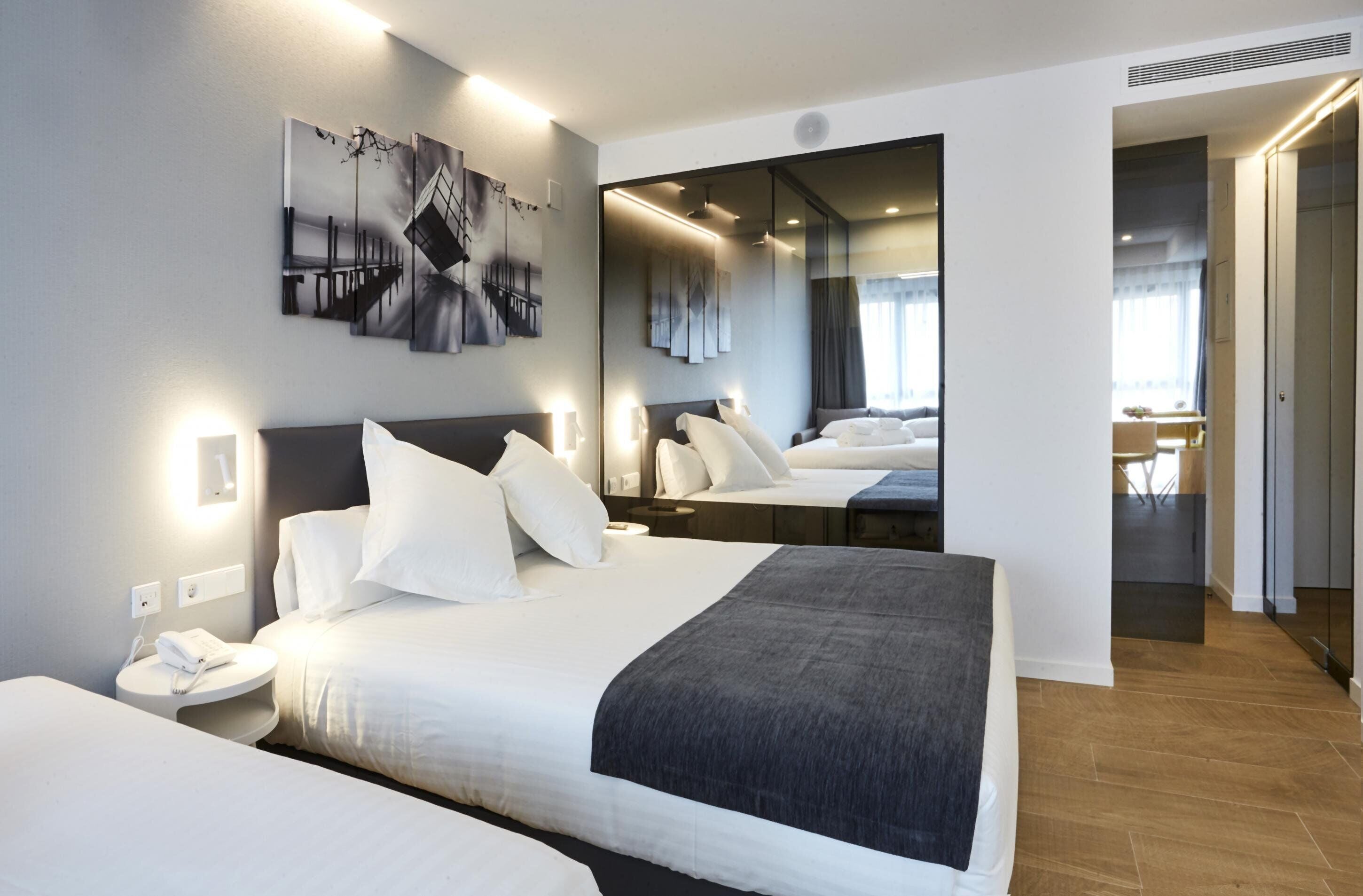 Una habitación de hotel moderna con una cama grande, mesitas de noche, un espejo y cuadros en la pared.