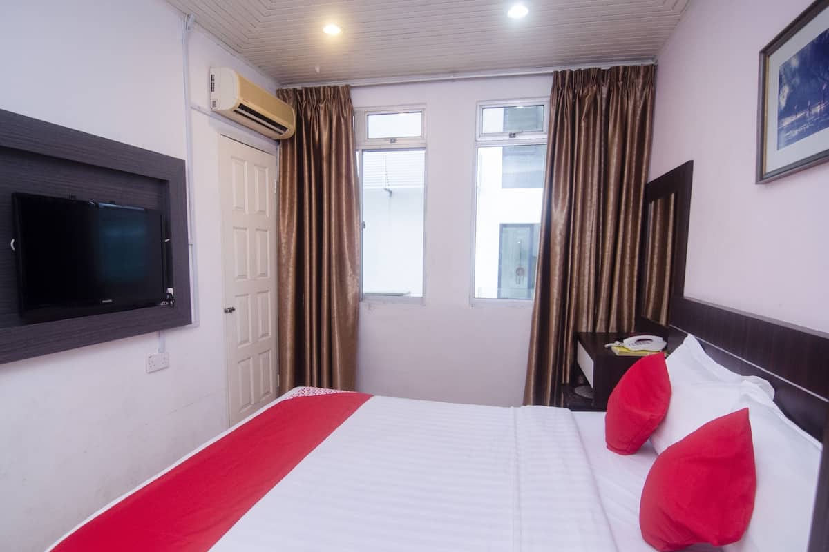 A hotel room with a bed, a television mounted on the wall, a window with curtains, and a bedside table with a phone.