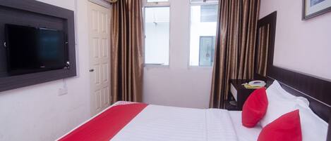 Habitación de hotel con una cama, televisión montada en la pared, una ventana con cortinas y una mesita de noche con teléfono.