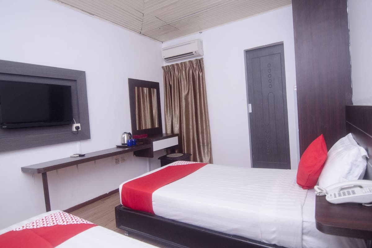 A hotel room with two beds, a TV, a desk with a phone, and an air conditioning unit.