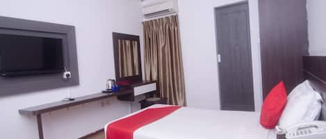 A hotel room with two beds, a TV, a desk with a phone, and an air conditioning unit.