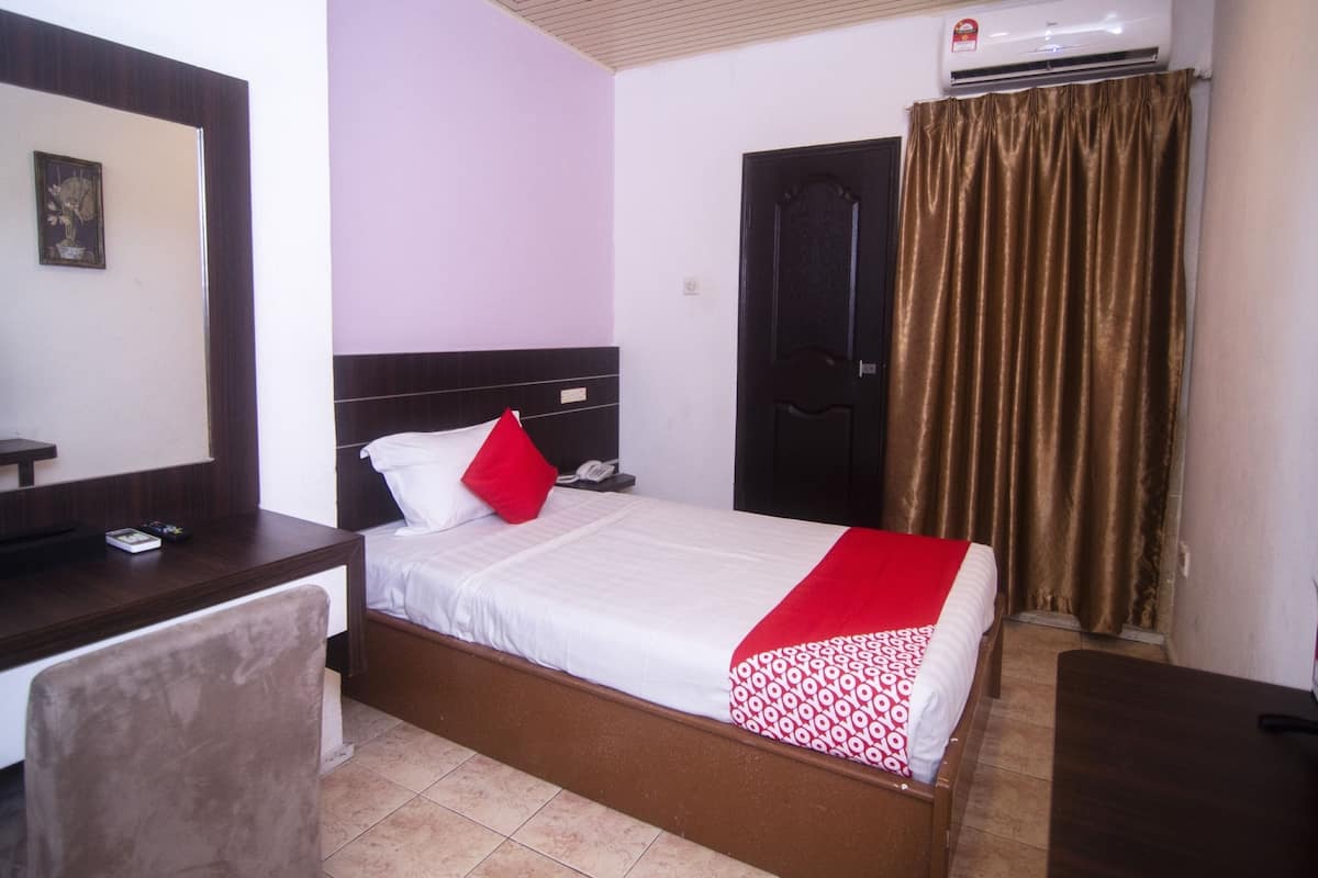 A hotel room with a bed, a desk, a chair, an air conditioner, and a door.