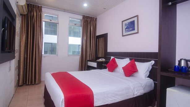 A hotel room with a bed, a nightstand, a desk, a chair, a window, curtains, a picture on the wall, and a radiator. - Hotel O yfair Hotel (Kuching)