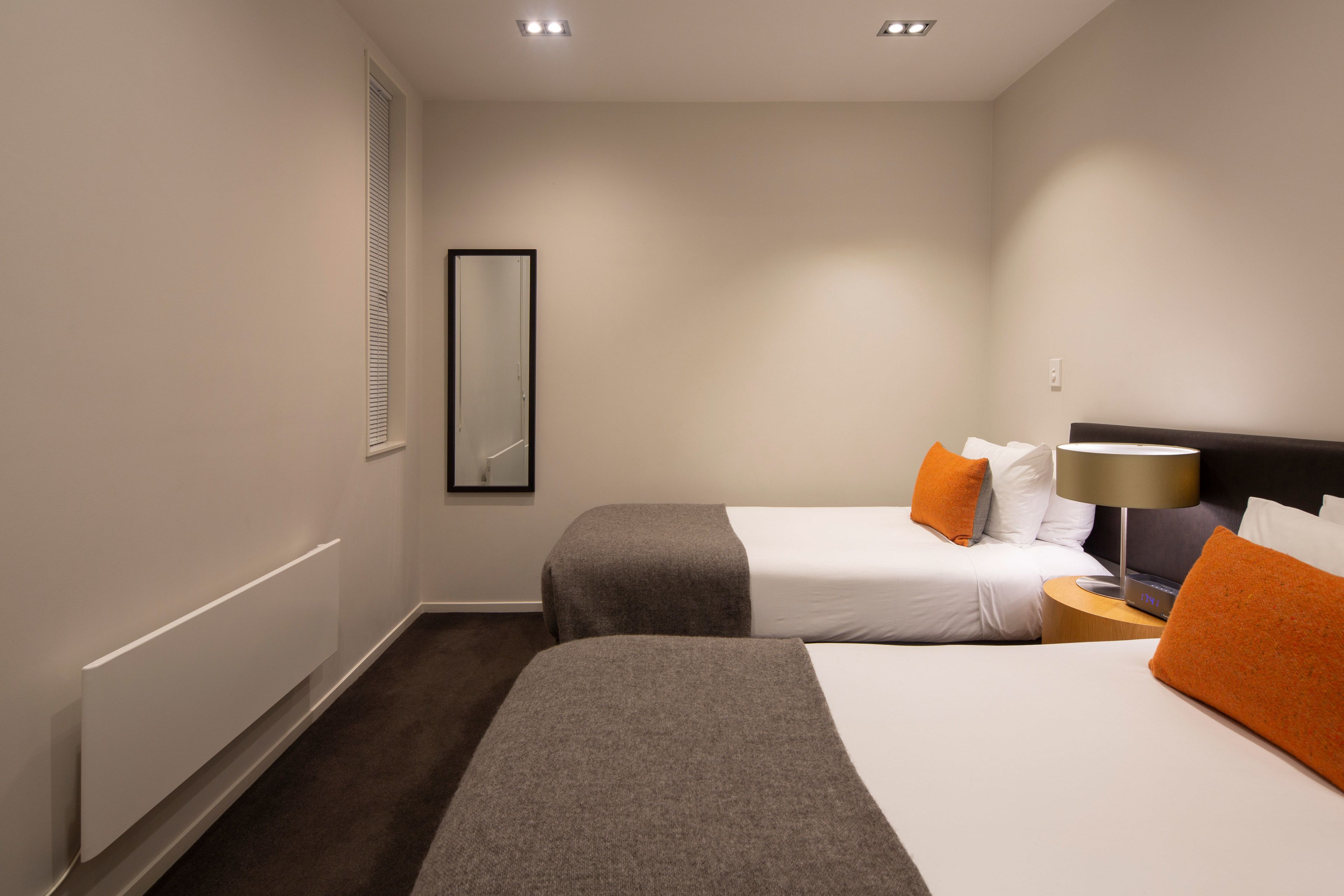 A hotel room with two beds, a nightstand, a lamp, and a mirror.