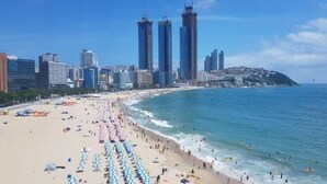 A beach with umbrellas and people, a city skyline with tall buildings, and a clear blue sky. - Browndot Hotel Centum City Bexco (Busan)