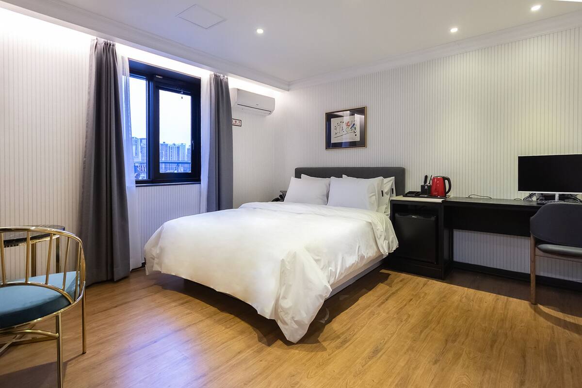 Una habitación de hotel con cama, escritorio, silla y ventana con cortinas.