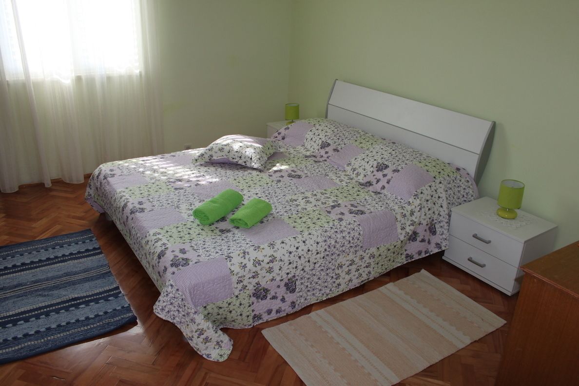 A bedroom with a bed, two nightstands, a window with curtains, and a patterned rug.