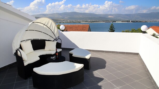 A rooftop terrace with a white umbrella seating area, a round table, and a view of a lake and mountains.