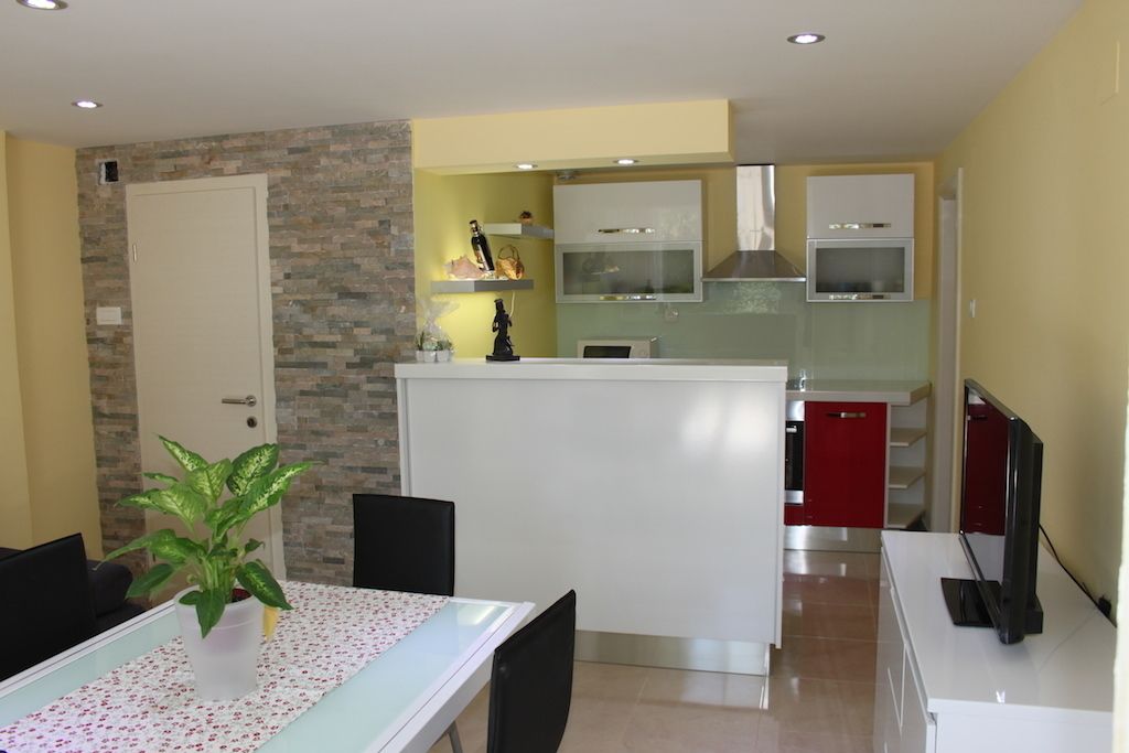 Uma cozinha moderna com ilha central, área de jantar com mesa e cadeiras, e uma TV em um suporte.