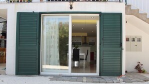A modern building with a sliding glass door entrance, a visible kitchen area, and a small outdoor seating area.