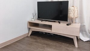 Ett TV-bord i trä med en platt-TV, en fjärrkontroll och en liten behållare med doftoljor och doftstavar.