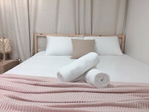 A neatly made bed with white linens and a pink knitted blanket, a wooden headboard, and a bedside lamp. - Myeongdong Sky Castle House (Seoul)