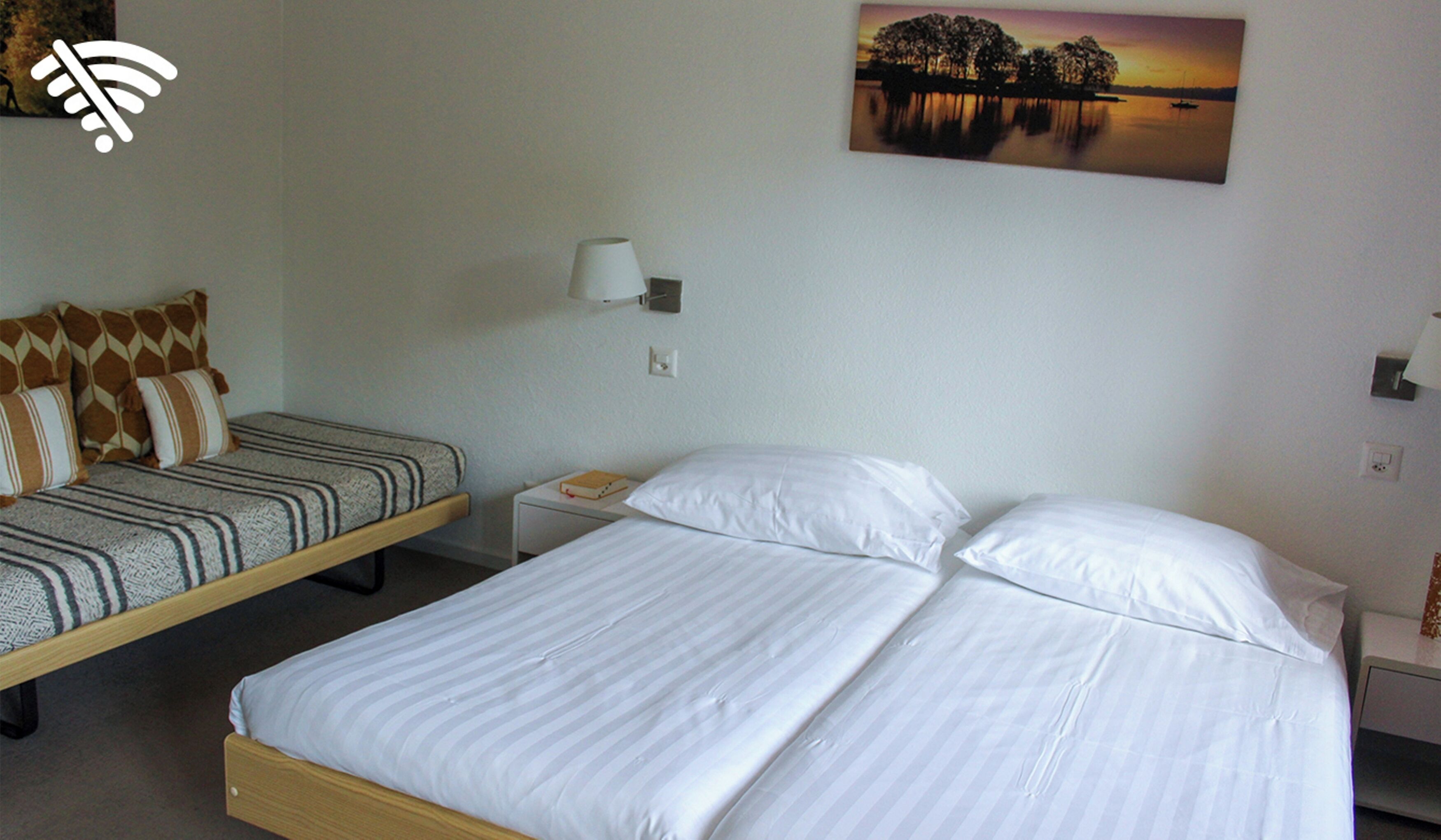 A hotel room with a bed, a sofa, a nightstand, and a painting on the wall.