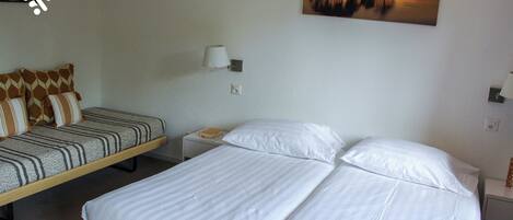 A hotel room with a bed, a sofa, a nightstand, and a painting on the wall.