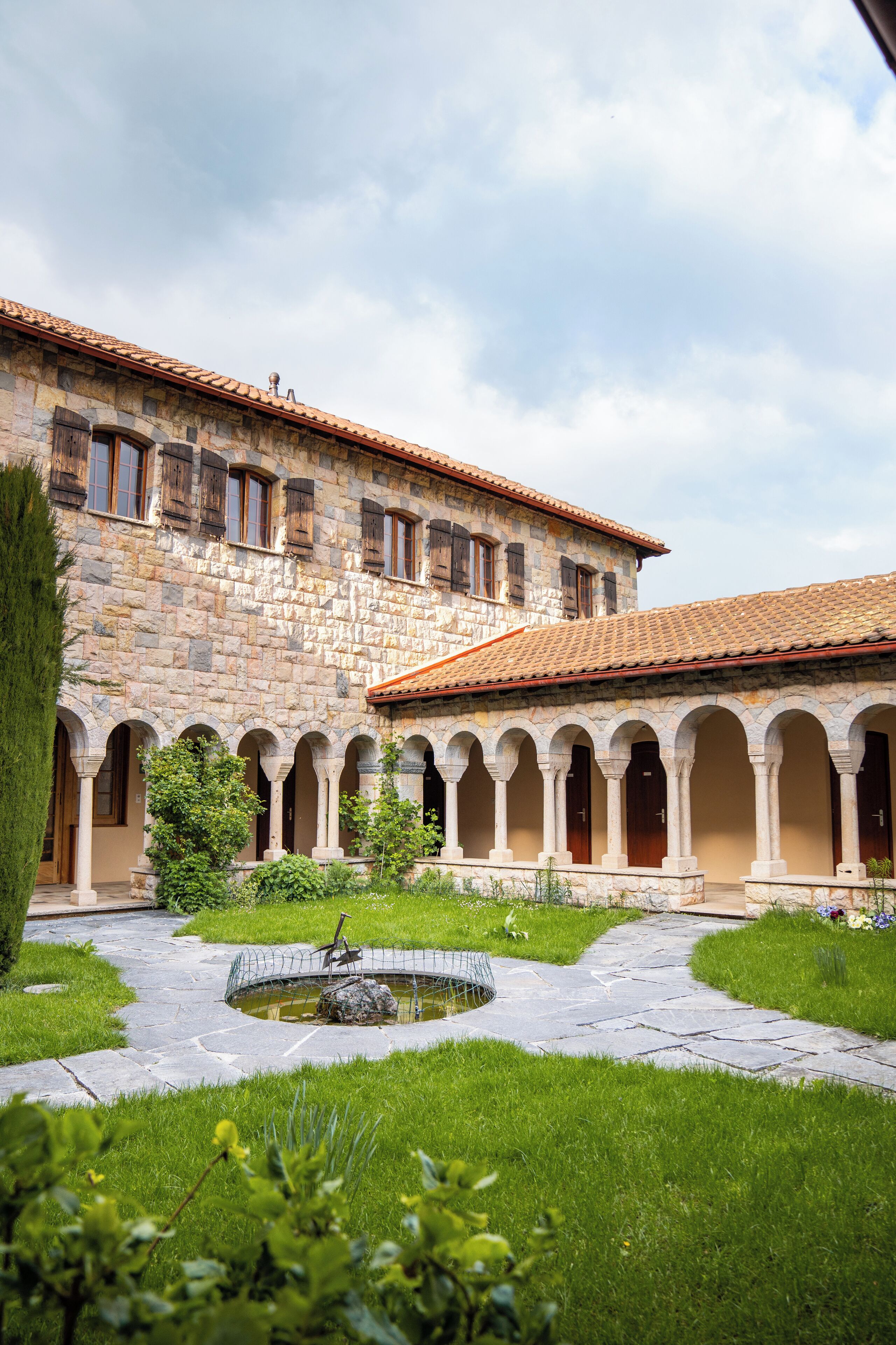 A courtyard with a stone building, arched walkways, and a central water feature.