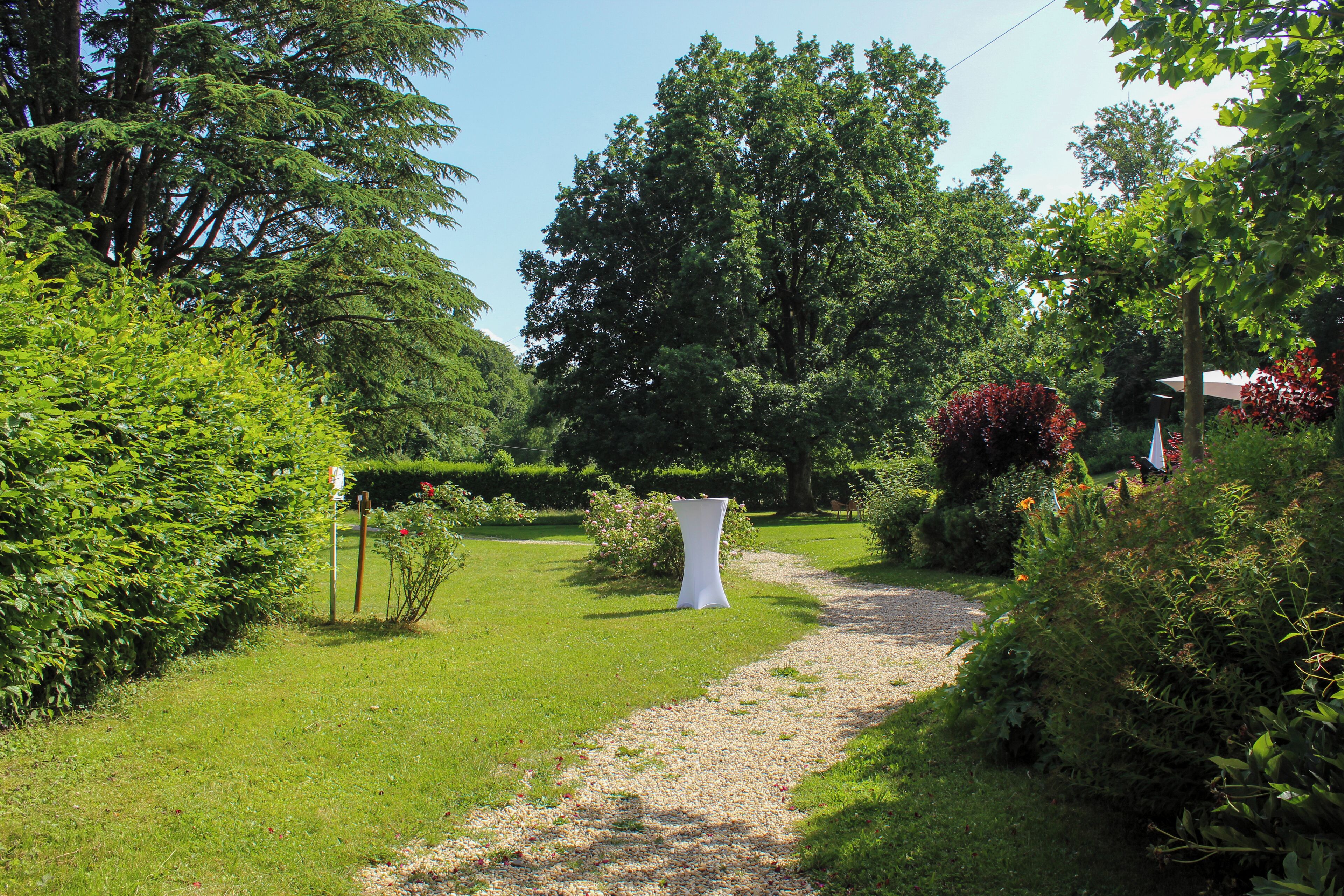 Un sendero en un jardín que lleva a una estructura blanca, rodeada de abundante vegetación y árboles.