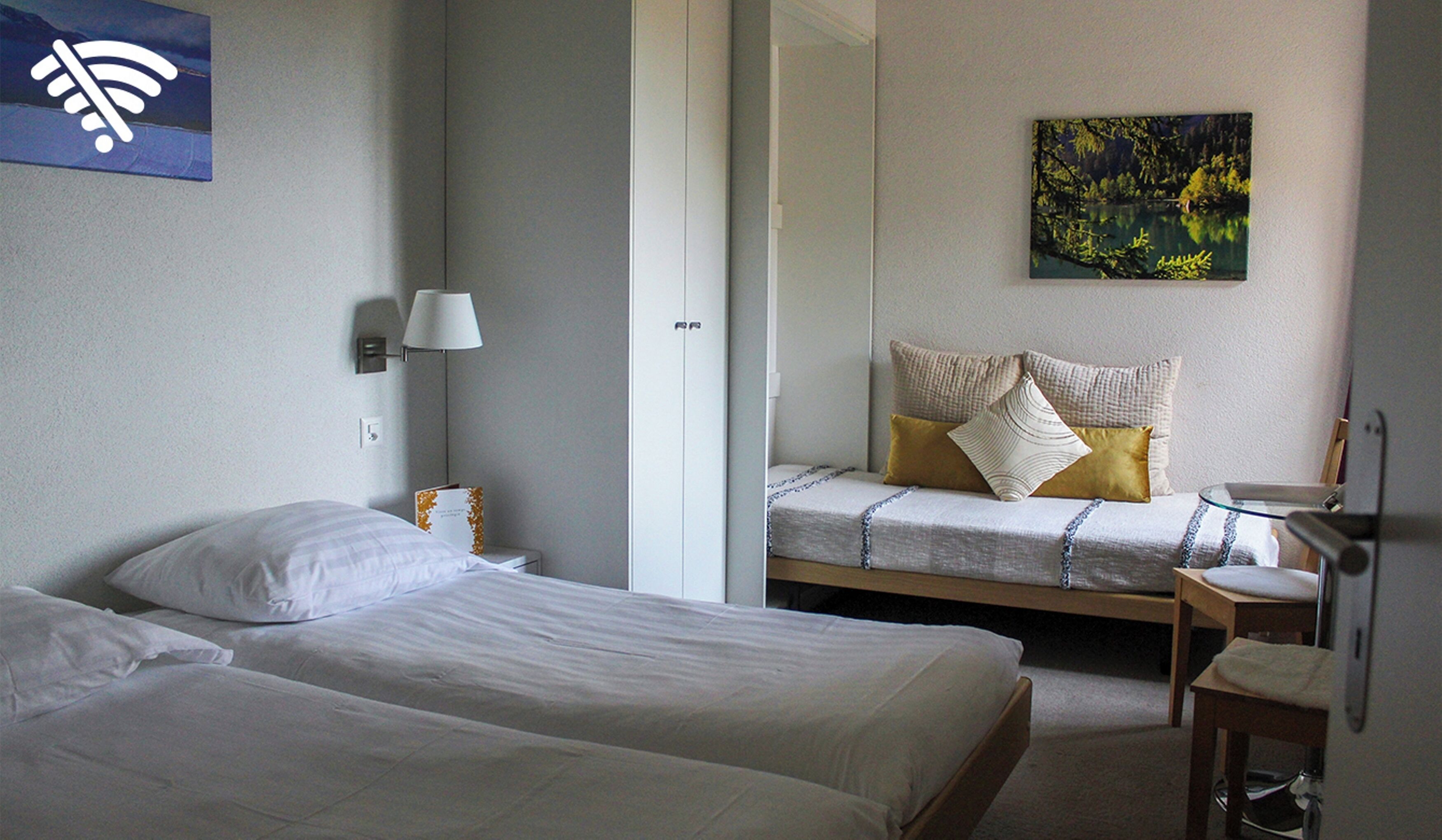 Ein Hotelzimmer mit zwei Betten, einem Nachttisch mit Lampe, einem Bild an der Wand und einem Stuhl.