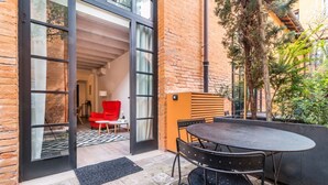 Un patio exterior moderno con una mesa redonda y sillas, una silla roja y una puerta de cristal que da a un espacio interior.