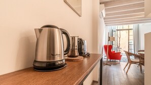 Una cocina con encimera de madera, hervidor de agua y cafetera. Hay una zona de comedor con una silla roja y una mesa.