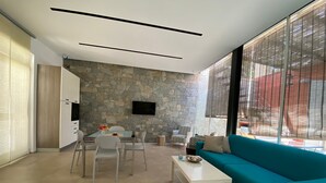 A modern living room with a stone wall, a teal sofa, a dining table with chairs, and a TV mounted on the wall. - VILLA BIANCA LOFT COMPLEX 1 (La Maddalena)