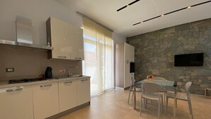 A modern kitchen with white cabinets, a built-in stove, and a stone wall. - VILLA BIANCA LOFT COMPLEX 1 (La Maddalena)