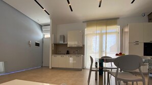 A modern kitchen with white cabinets, a dining area with a table and chairs, and a view of the sea through large windows. - VILLA BIANCA LOFT COMPLEX 1 (La Maddalena)