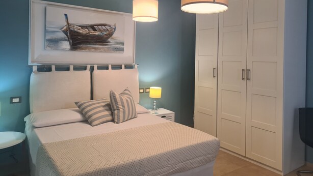 Un dormitorio con cama, mesita de noche, lámpara, armario y un cuadro en la pared.