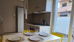 Un comedor con una mesa blanca dispuesta para cuatro personas, sillas amarillas y una cocina al fondo.