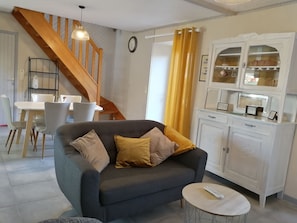 A living room with a grey sofa, a wooden staircase, a dining area with a white table and chairs, and a white cabinet with glass doors. - Frehel: country holiday homes - 4 rooms - 1/6 persons (Frehel)