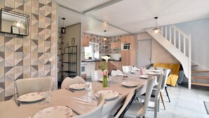 A dining area with a long table set for six, a kitchen in the background, and a staircase leading to an upper level. - Frehel: country holiday homes - 4 rooms - 1/6 persons (Frehel)