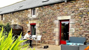 A stone building with a red door, outdoor seating, and a dog lying on the ground. - Frehel: country holiday homes - 4 rooms - 1/6 persons (Frehel)