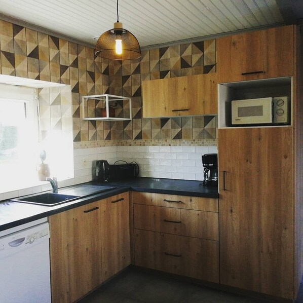 A kitchen with wooden cabinets, a microwave, a coffee maker, and a hanging light fixture.