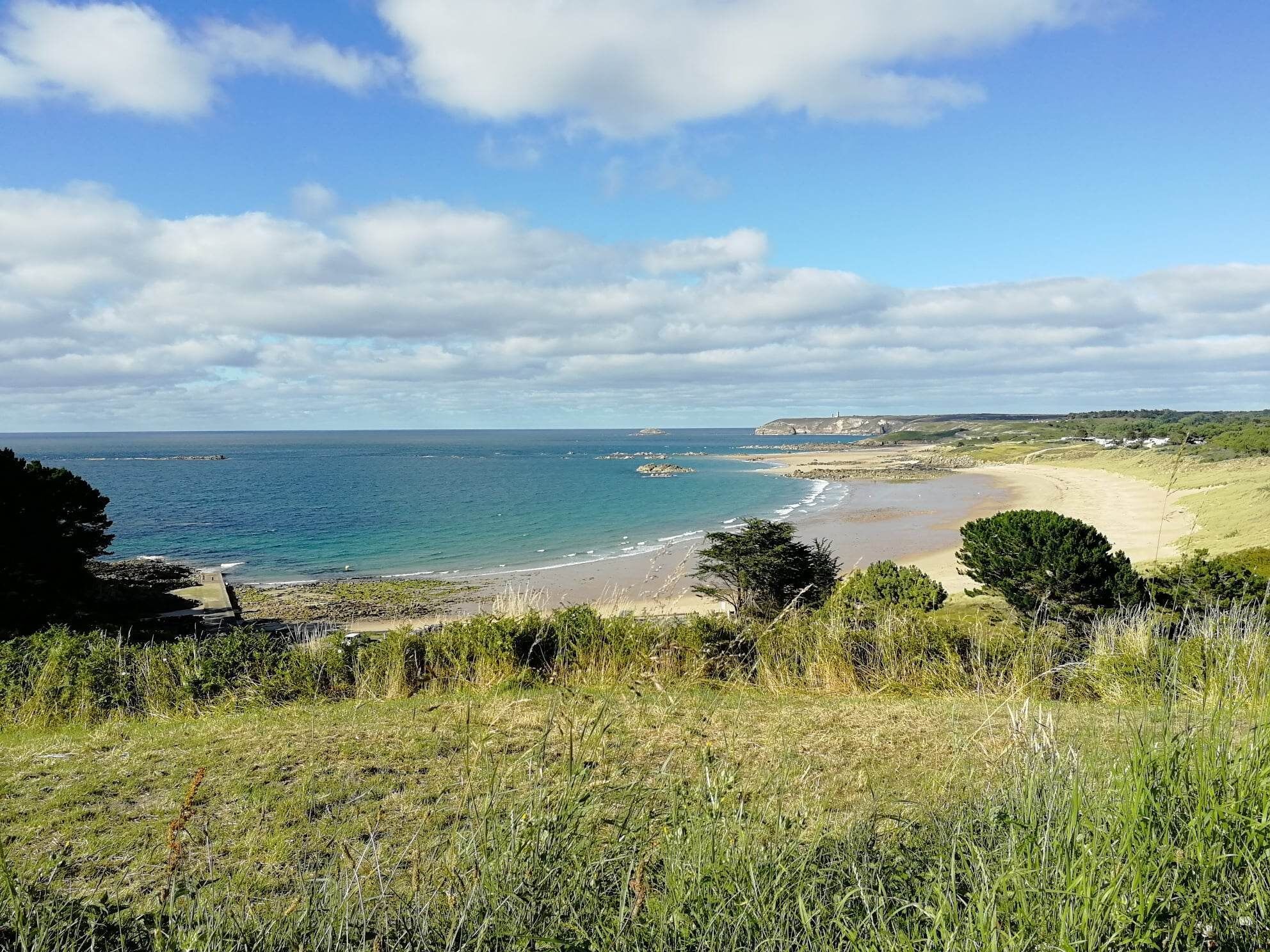 A coastal landscape with a sandy beach, grassy areas, and a clear view of the sea.