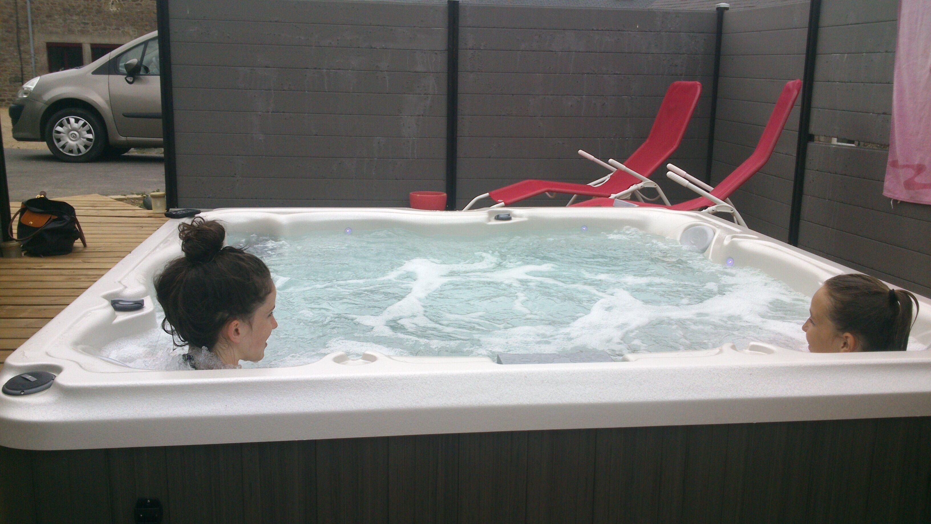 A hot tub with two people in it, a red lounge chair, and a car parked outside.