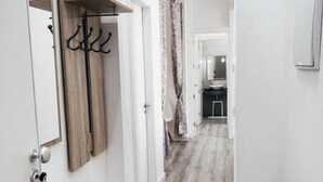 A hallway with a wooden floor, a coat rack, a mirror, and a door leading to a bathroom.