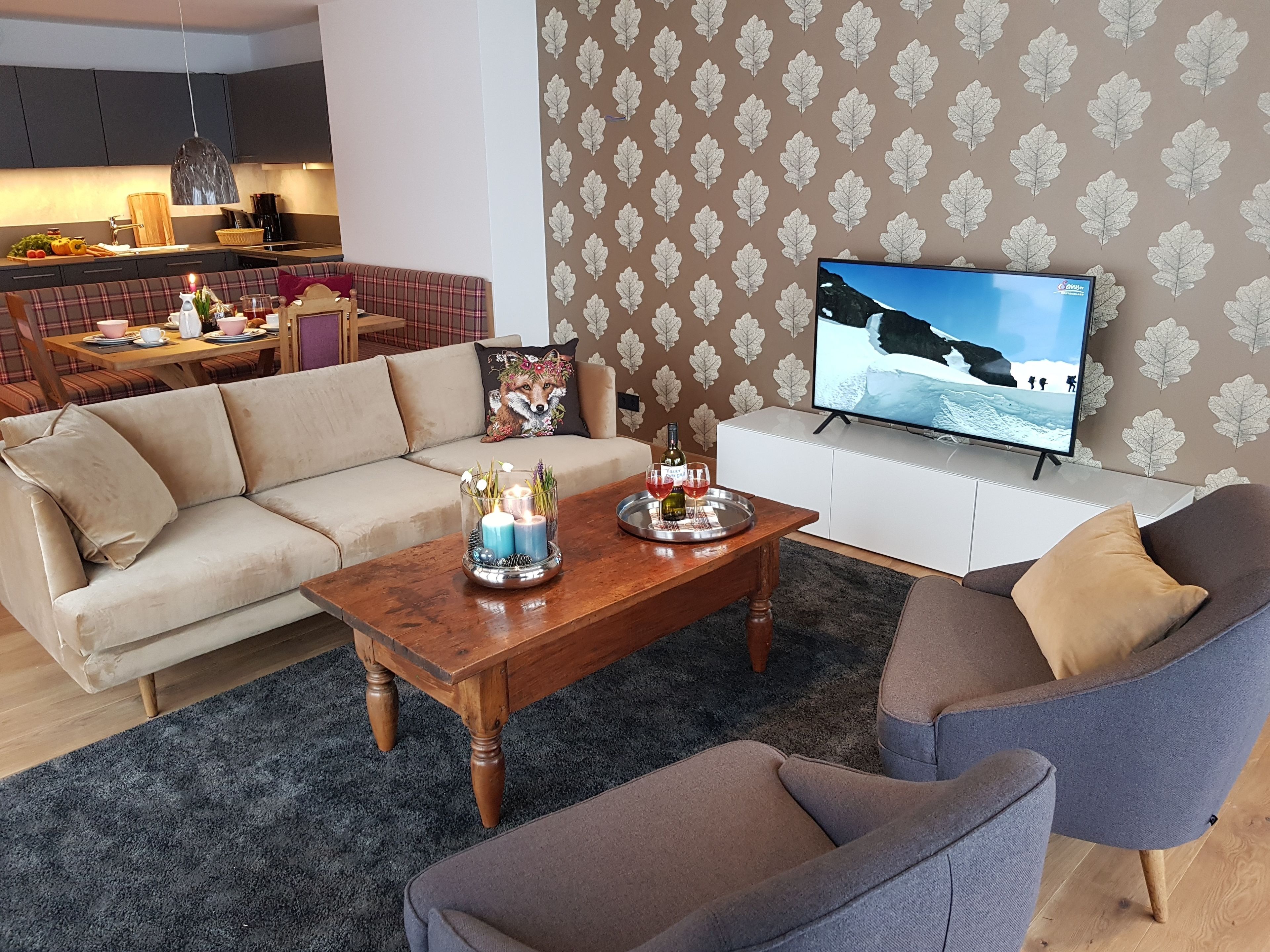 Un salon moderne avec un canapé, une table basse ornée de bougies et un téléviseur diffusant un paysage de montagne.