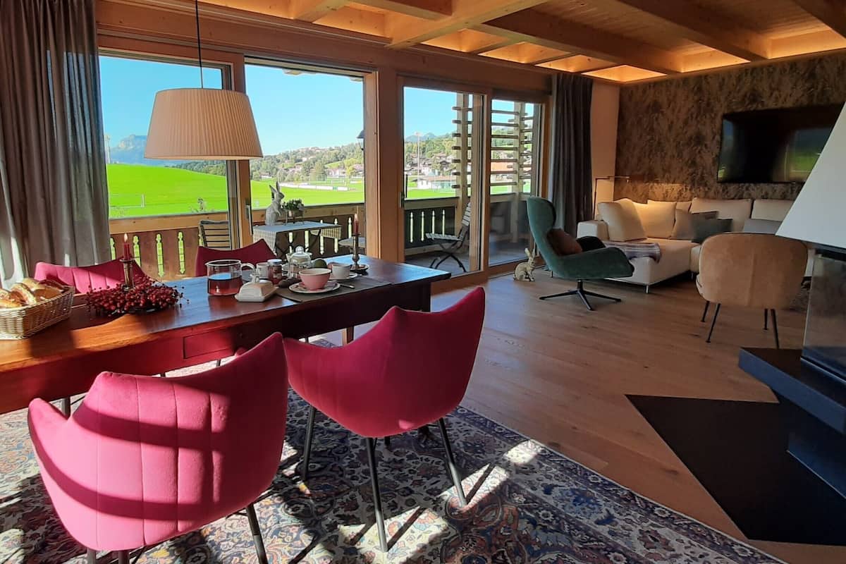 A spacious living area with a wooden ceiling, a dining table set with red chairs, a sofa, and a TV.