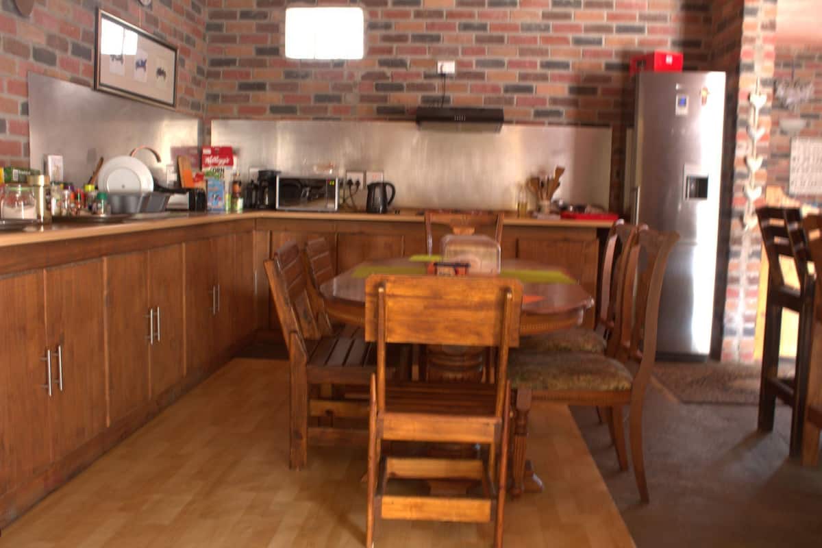 A kitchen with wooden cabinets, a dining table with chairs, a refrigerator, and a brick wall.