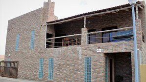 Un edificio de ladrillo de dos pisos con balcón, entrada con reja y un pequeño porche.