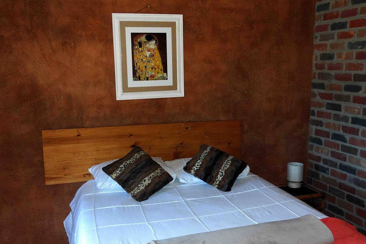A bed with a wooden headboard, two pillows, a white bedspread, and a red blanket.