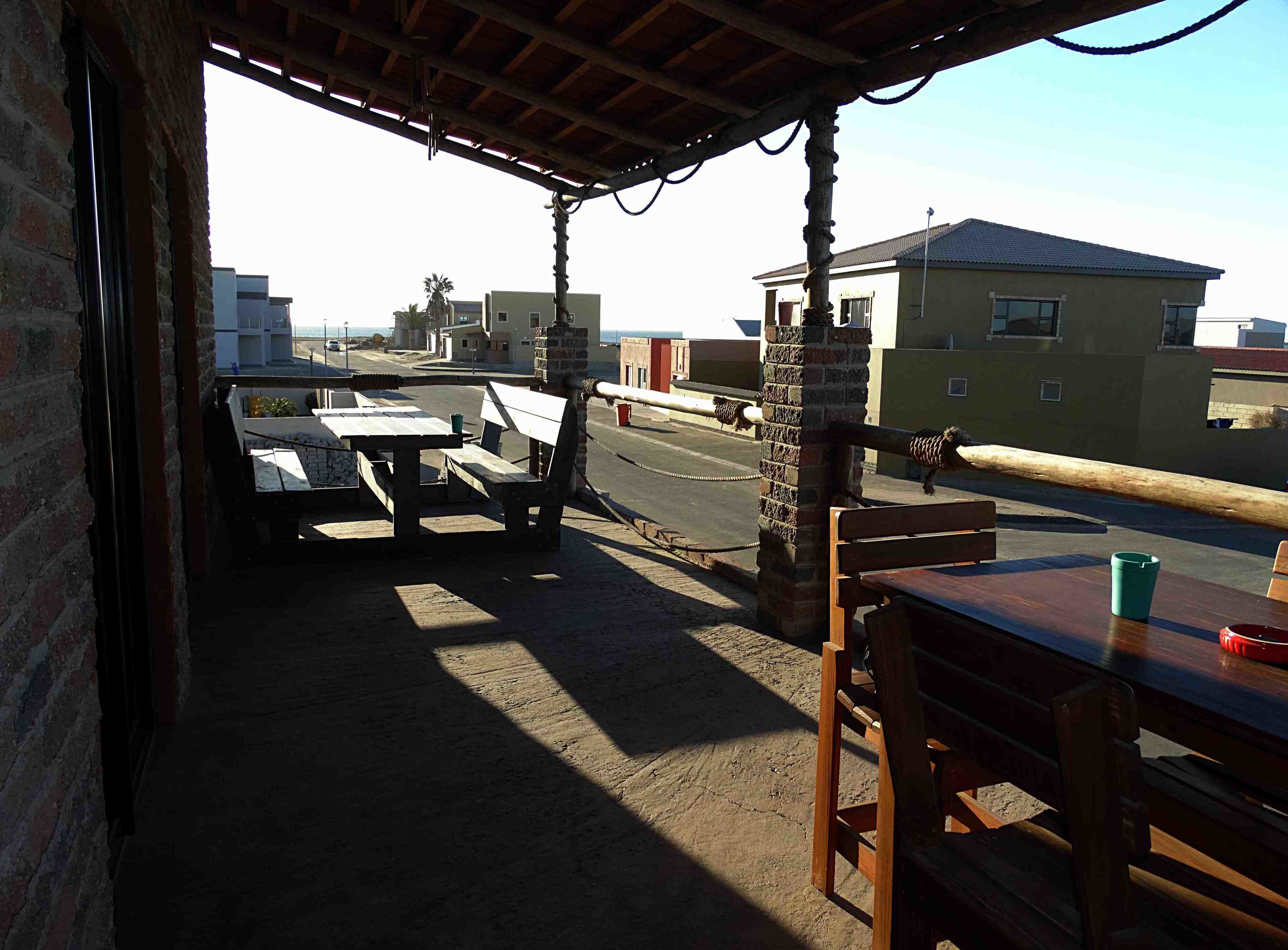 Un espacio al aire libre techado con mesas y bancos, un pilar de ladrillo y vistas de edificios al fondo.