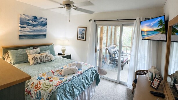 Ein Schlafzimmer mit einem Bett, einem Deckenventilator, einem Fernseher, einem Schreibtisch und Blick ins Freie.