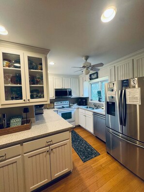 Une cuisine moderne avec des meubles blancs, des appareils en acier inoxydable et un ventilateur de plafond.