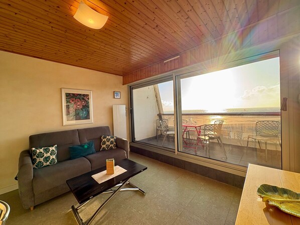 Un salon moderne avec un canapé, une table basse et une grande fenêtre donnant sur une plage.