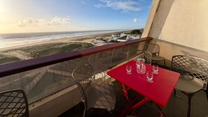A balcony with a red table and chairs, overlooking a beach and ocean.